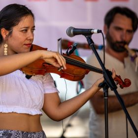 One person playing violin in the foreground, another in the background playing a Gaita galega